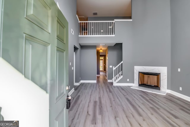 foyer entrance featuring a fireplace, a towering ceiling, and light wood-type flooring
