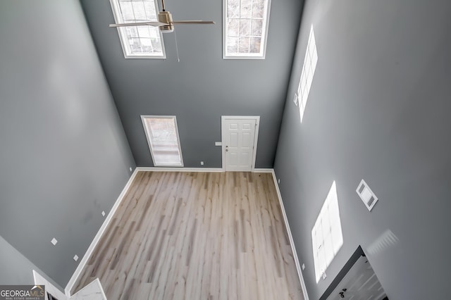 unfurnished living room featuring ceiling fan, a towering ceiling, and light hardwood / wood-style floors
