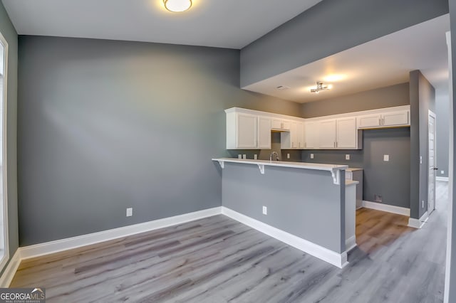 kitchen featuring a breakfast bar, kitchen peninsula, white cabinetry, and light hardwood / wood-style flooring