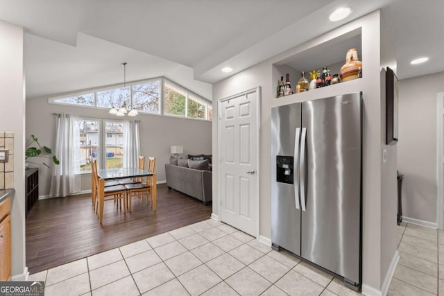 kitchen featuring lofted ceiling, an inviting chandelier, decorative light fixtures, light tile patterned flooring, and stainless steel fridge with ice dispenser