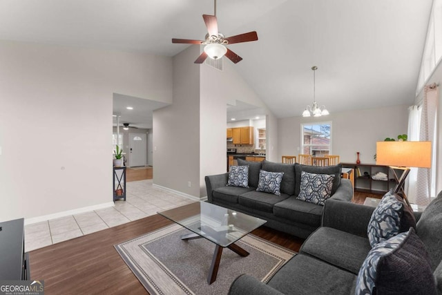 living room with ceiling fan with notable chandelier, high vaulted ceiling, and light hardwood / wood-style flooring