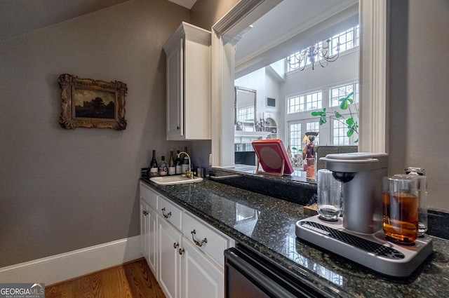 kitchen with french doors, sink, wood-type flooring, dark stone countertops, and white cabinetry