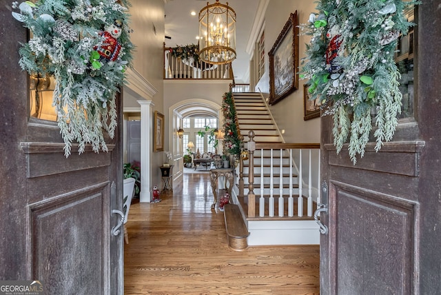 entrance foyer featuring hardwood / wood-style floors, a towering ceiling, crown molding, and an inviting chandelier