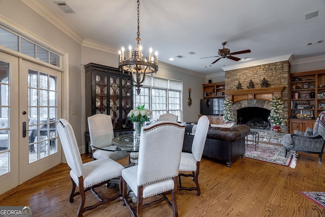 dining space with a stone fireplace, crown molding, ceiling fan with notable chandelier, and hardwood / wood-style flooring