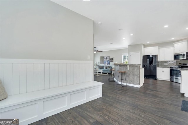 interior space featuring a center island, ceiling fan, appliances with stainless steel finishes, a kitchen bar, and white cabinetry