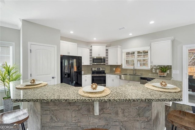 kitchen with light stone counters, stainless steel appliances, sink, white cabinetry, and a breakfast bar area