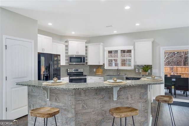 kitchen with a breakfast bar, sink, light stone counters, white cabinetry, and stainless steel appliances