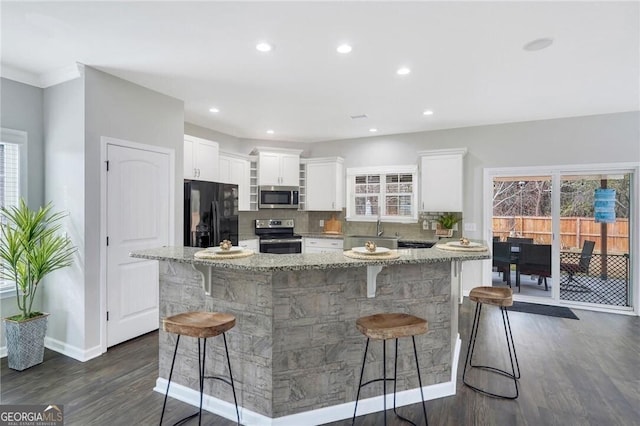 kitchen featuring a kitchen bar, light stone countertops, a healthy amount of sunlight, and stainless steel appliances