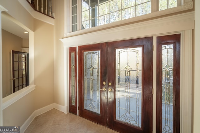 foyer entrance featuring tile patterned floors, a healthy amount of sunlight, a towering ceiling, and french doors