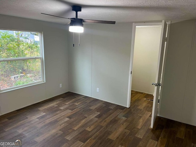 empty room with a textured ceiling, dark hardwood / wood-style flooring, plenty of natural light, and ceiling fan