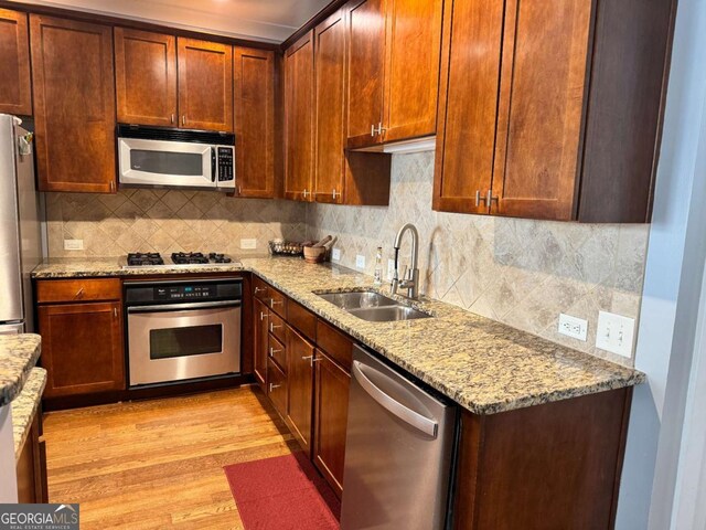 kitchen with light stone countertops, tasteful backsplash, stainless steel appliances, sink, and light hardwood / wood-style floors