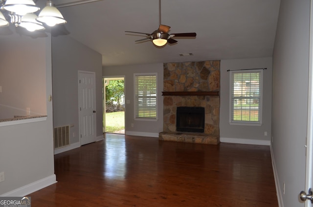 unfurnished living room with lofted ceiling, ceiling fan with notable chandelier, a stone fireplace, dark hardwood / wood-style floors, and a wealth of natural light