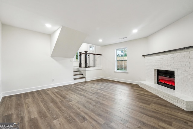 unfurnished living room with a brick fireplace and dark hardwood / wood-style floors