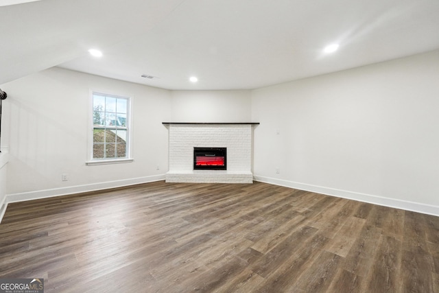 unfurnished living room featuring a brick fireplace and dark hardwood / wood-style flooring