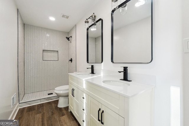 bathroom with hardwood / wood-style flooring, vanity, tiled shower, and toilet