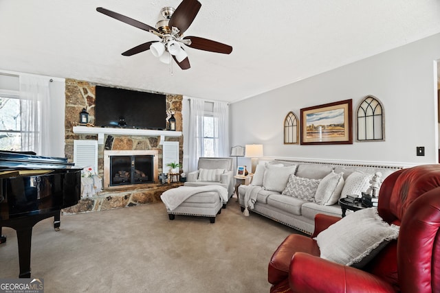 carpeted living room with a stone fireplace and ceiling fan