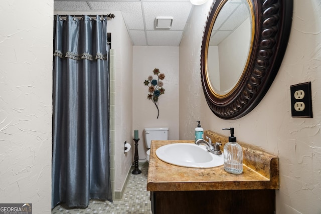 bathroom with tile patterned floors, a drop ceiling, toilet, and vanity