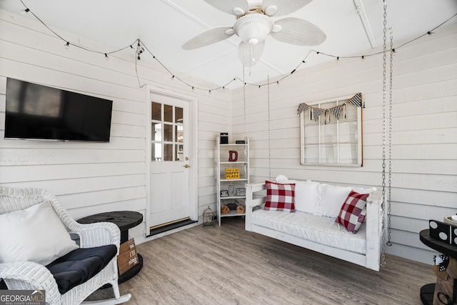 living area featuring wood-type flooring, ceiling fan, and wood walls