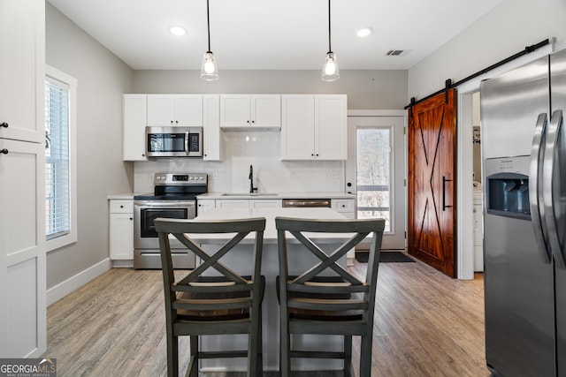 kitchen with sink, a barn door, decorative light fixtures, white cabinetry, and stainless steel appliances