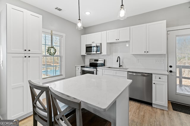 kitchen featuring white cabinets, appliances with stainless steel finishes, decorative light fixtures, and sink