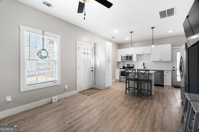 kitchen with hanging light fixtures, stainless steel appliances, a kitchen island, a breakfast bar area, and white cabinets