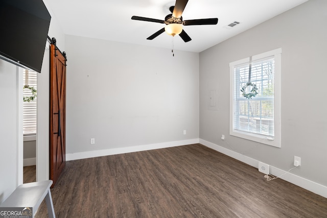 spare room featuring ceiling fan, a barn door, and dark wood-type flooring