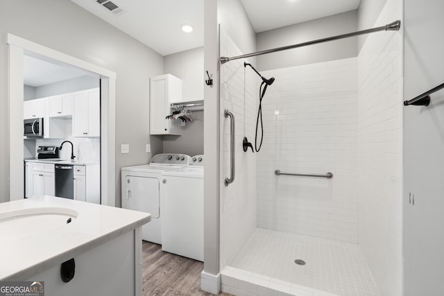 bathroom with hardwood / wood-style floors, vanity, backsplash, independent washer and dryer, and tiled shower