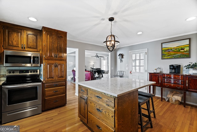 kitchen with stainless steel appliances, decorative light fixtures, a kitchen island, ceiling fan with notable chandelier, and ornamental molding