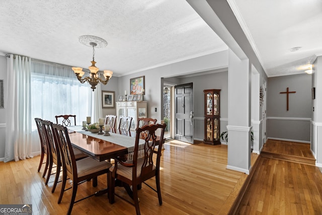 dining area featuring ornamental molding, light hardwood / wood-style floors, a textured ceiling, and a notable chandelier