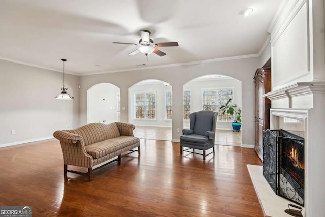 living room featuring a high end fireplace, dark wood-type flooring, ceiling fan, and crown molding