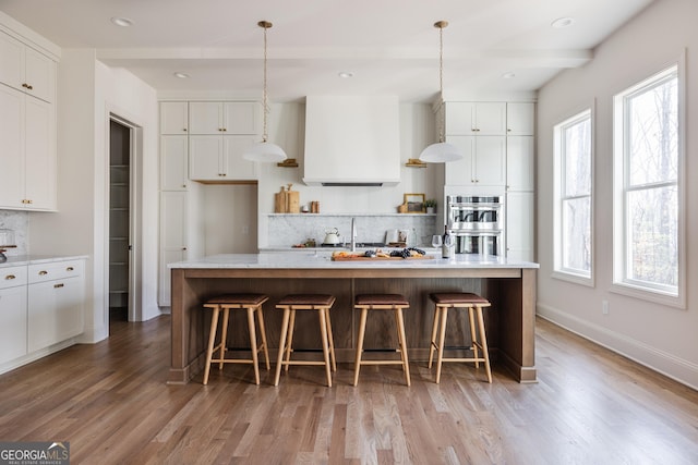 kitchen featuring wall chimney exhaust hood, a center island with sink, and white cabinets