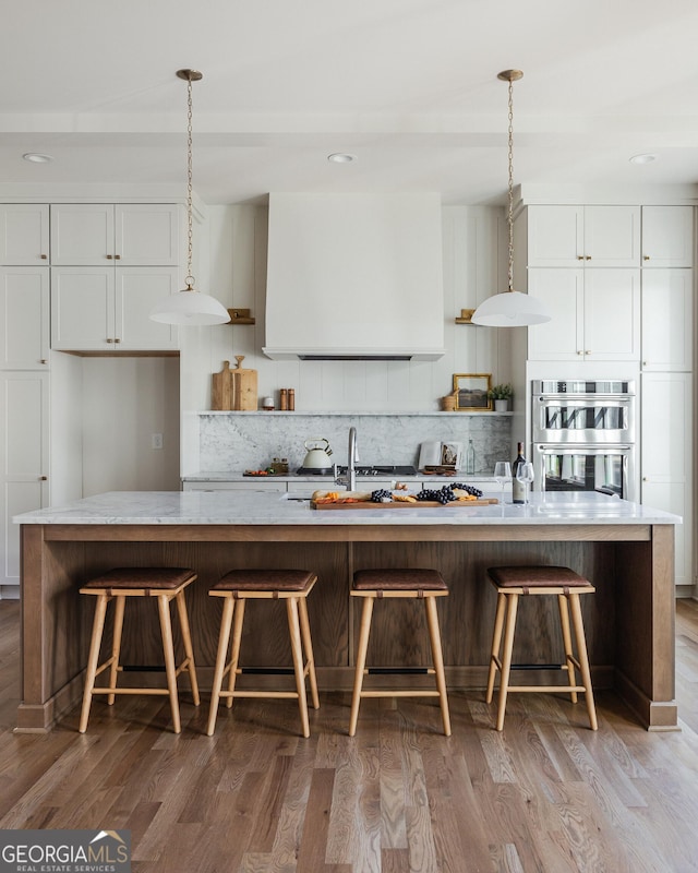 kitchen with white cabinetry, an island with sink, and stainless steel double oven