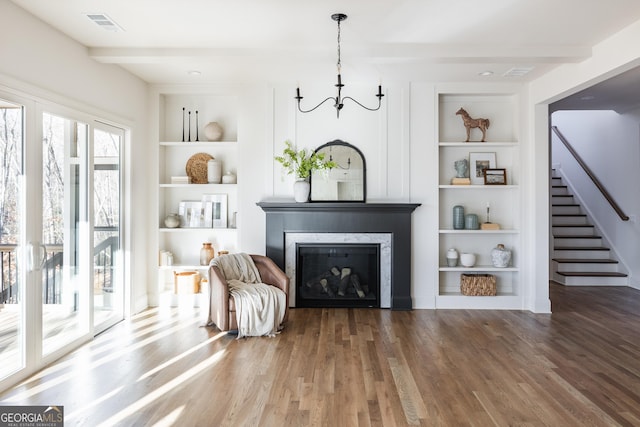 living area featuring beamed ceiling, wood-type flooring, a fireplace, and built in shelves