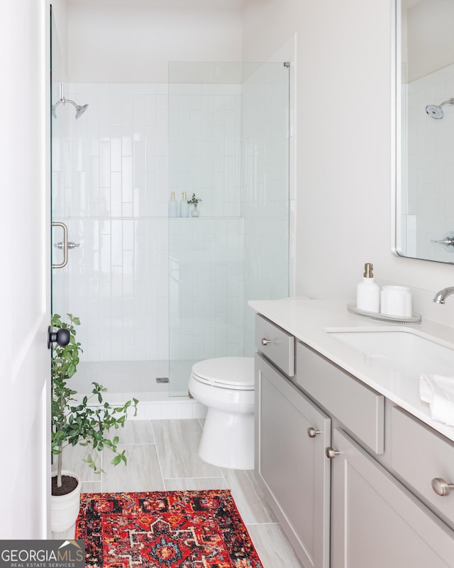 bathroom featuring a shower with door, vanity, and toilet