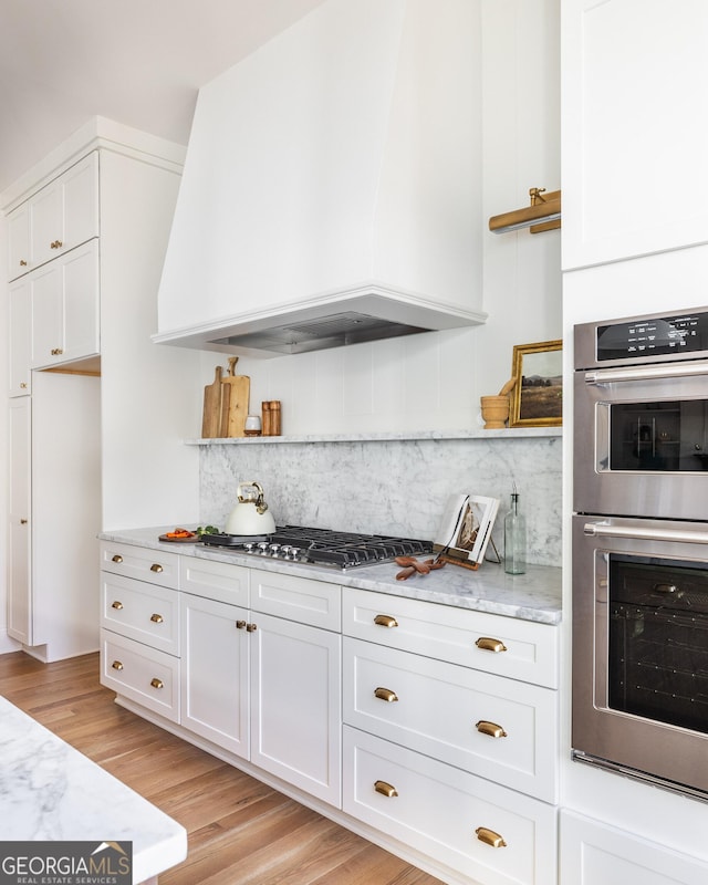 kitchen with white cabinetry, appliances with stainless steel finishes, light stone counters, and custom exhaust hood