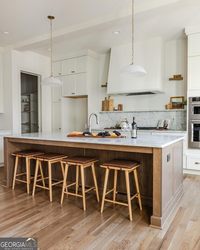 kitchen featuring double oven, backsplash, a spacious island, white cabinets, and a kitchen bar