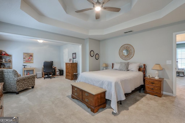 bedroom featuring a raised ceiling, light carpet, and ceiling fan