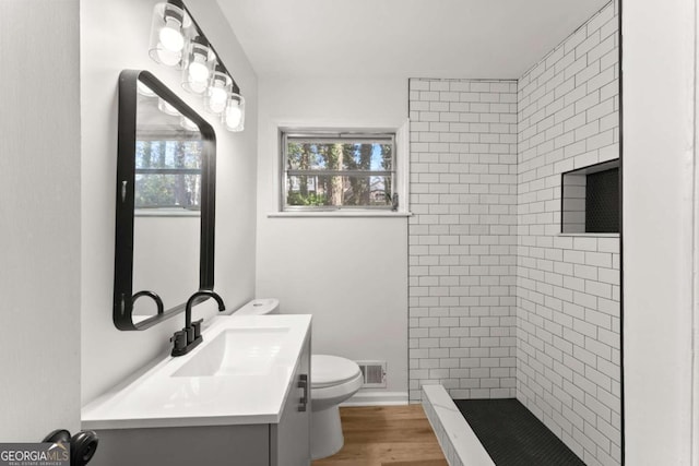 bathroom with a tile shower, vanity, toilet, and wood-type flooring