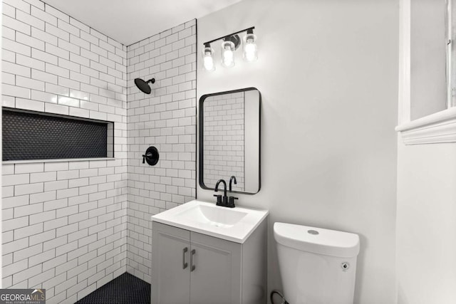 bathroom with a tile shower, vanity, and toilet