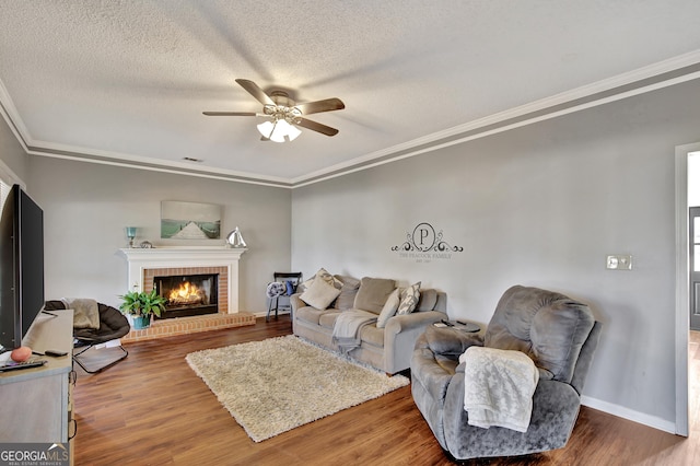 living room with ceiling fan, a brick fireplace, ornamental molding, a textured ceiling, and hardwood / wood-style flooring