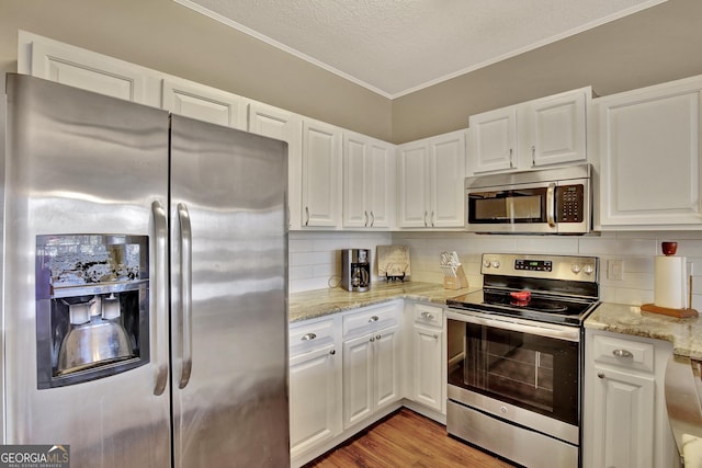 kitchen with light wood-type flooring, appliances with stainless steel finishes, backsplash, and white cabinetry