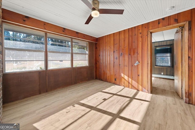 spare room with wooden walls, ceiling fan, light wood-type flooring, and a baseboard heating unit