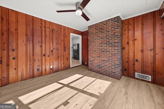 spare room with crown molding, ceiling fan, wood walls, and light wood-type flooring