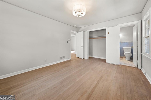 unfurnished bedroom with a closet, light wood-type flooring, and ensuite bath