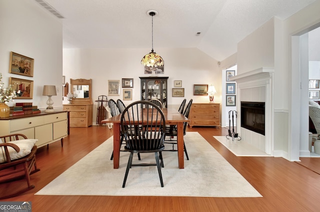 dining area with a textured ceiling, hardwood / wood-style floors, lofted ceiling, and a notable chandelier