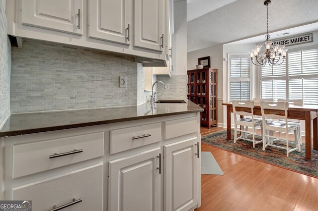 kitchen with an inviting chandelier, white cabinets, ventilation hood, decorative light fixtures, and stainless steel appliances