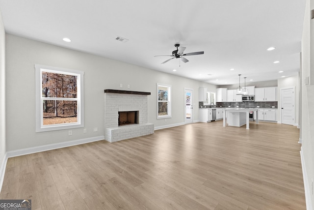 unfurnished living room with ceiling fan, a fireplace, and light wood-type flooring