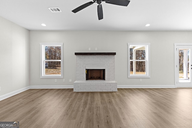 unfurnished living room with ceiling fan, light wood-type flooring, and a brick fireplace