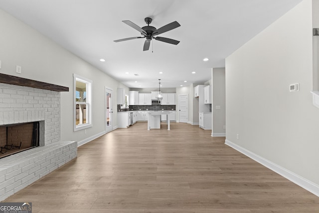 unfurnished living room with ceiling fan, light hardwood / wood-style flooring, sink, and a brick fireplace