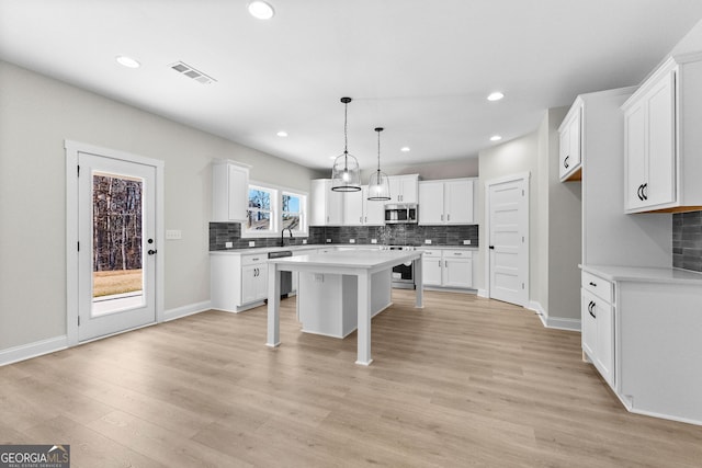 kitchen with a center island, plenty of natural light, pendant lighting, white cabinets, and appliances with stainless steel finishes